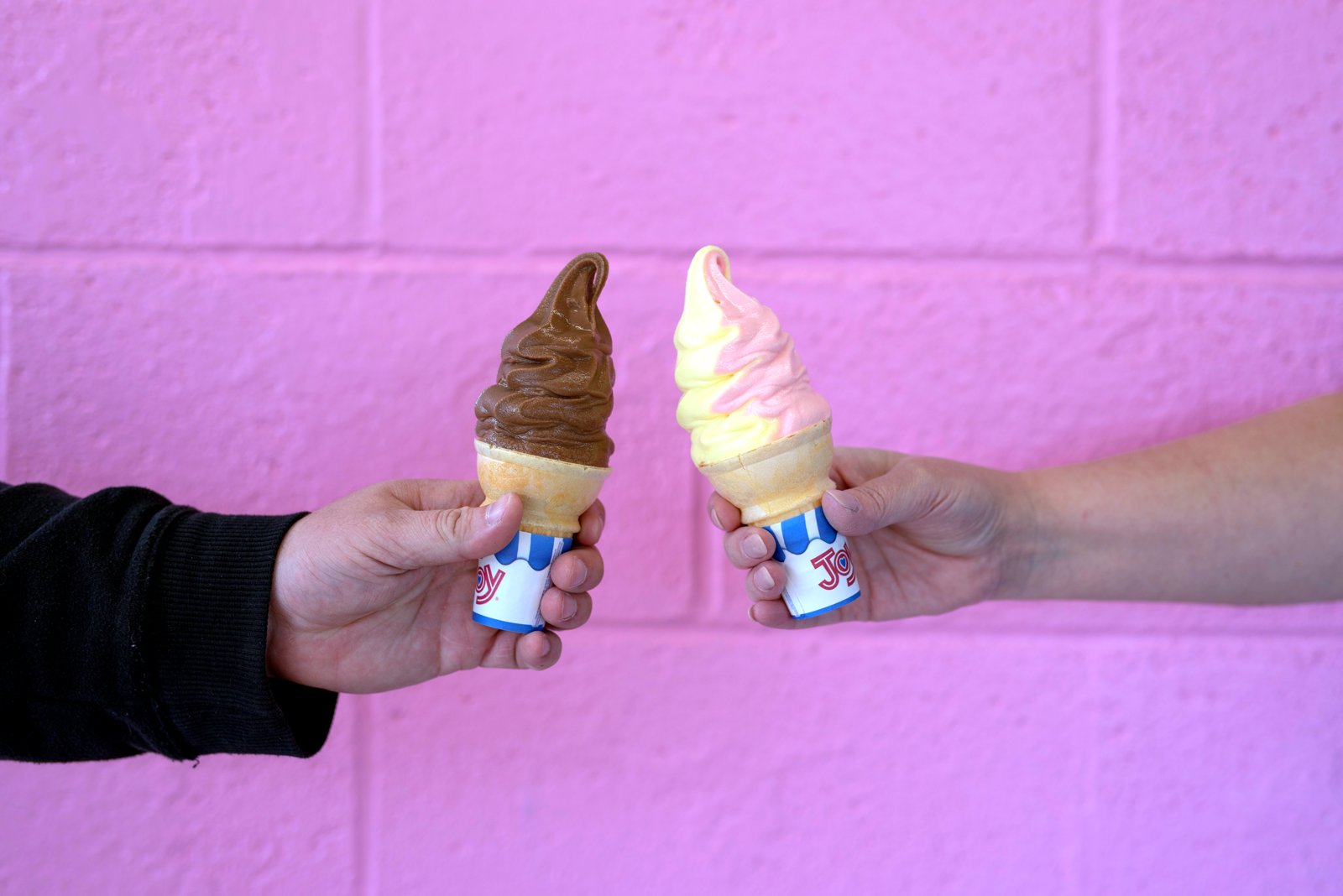Two soft serve cones held up against the pink wall