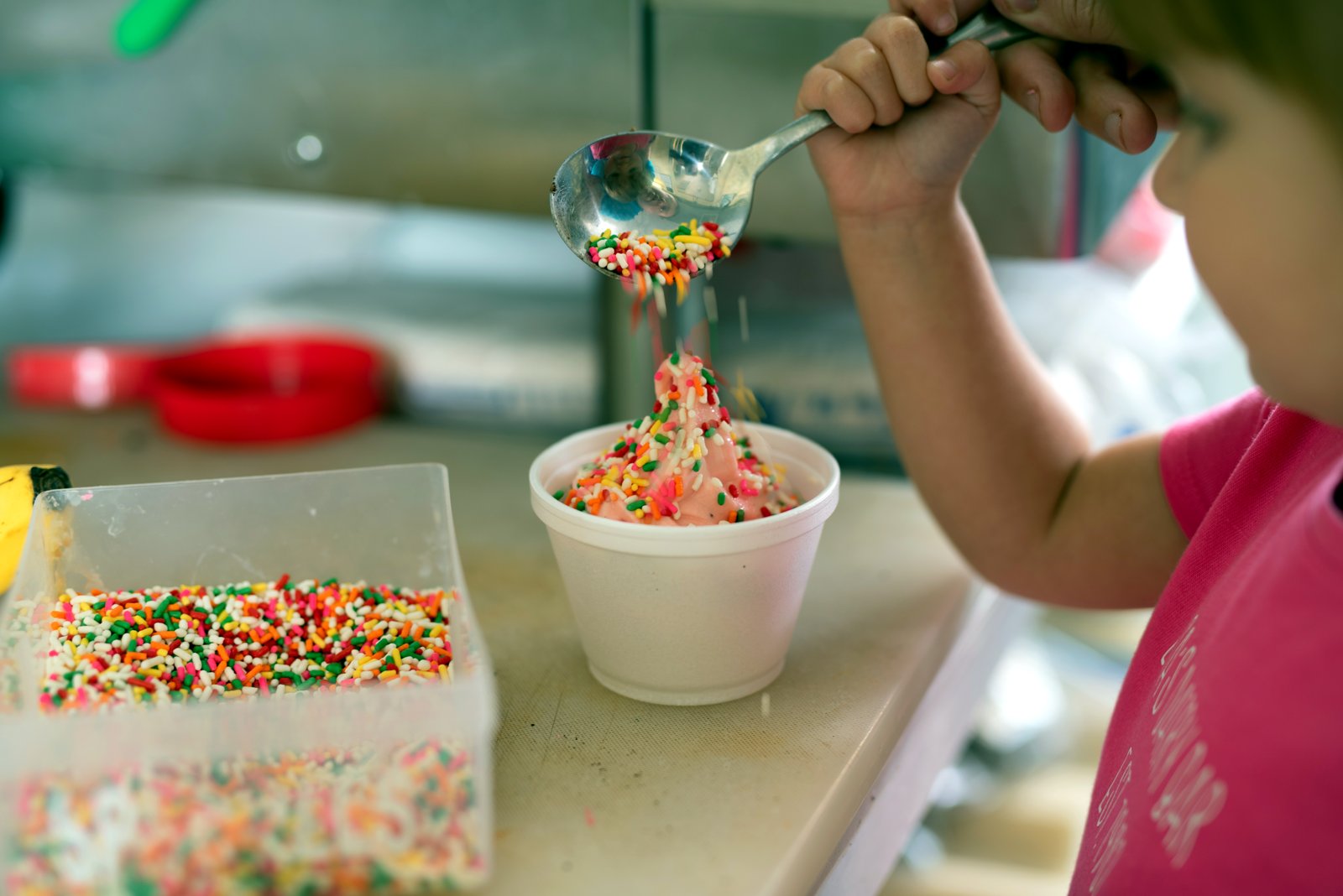 Sprinkles being spooned over a fresh cup of soft serve